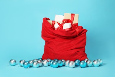 Photo of Santa Claus bag with baubles and gift boxes on light blue background