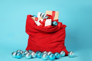 Photo of Santa Claus bag with baubles and gift boxes on light blue background