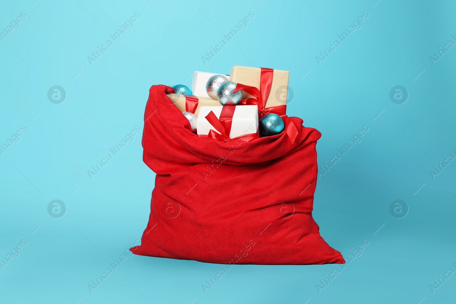 Photo of Santa Claus bag with baubles and gift boxes on light blue background