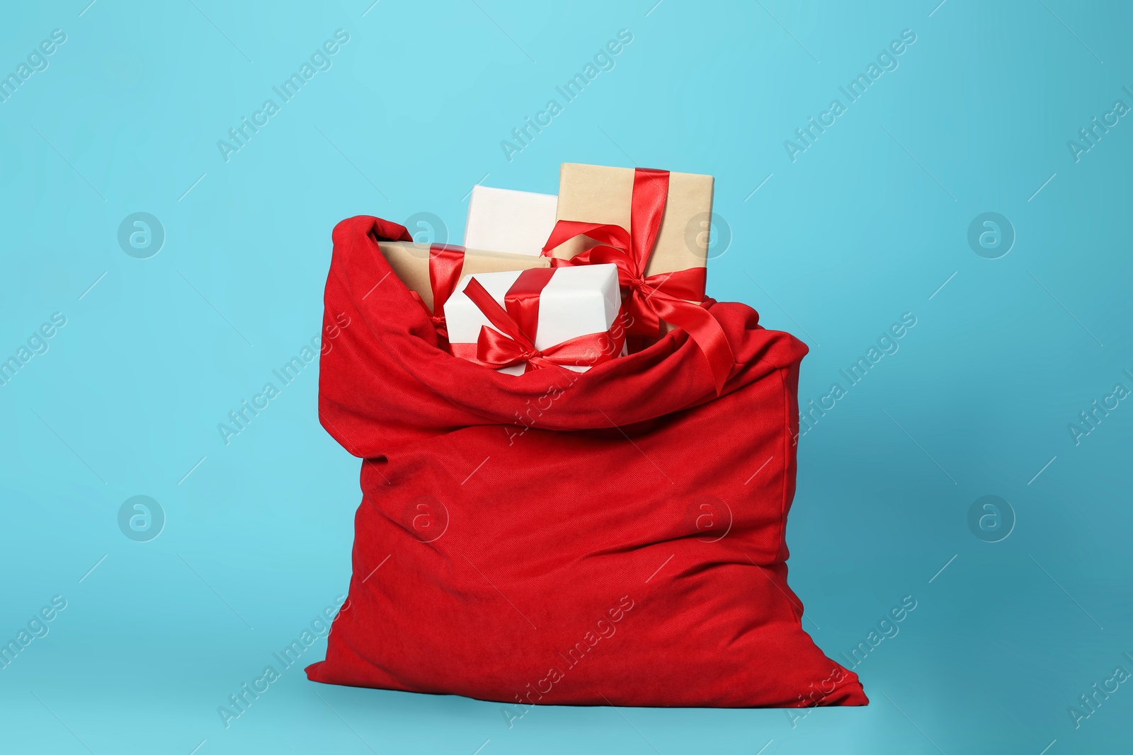 Photo of Santa Claus bag with gift boxes on light blue background