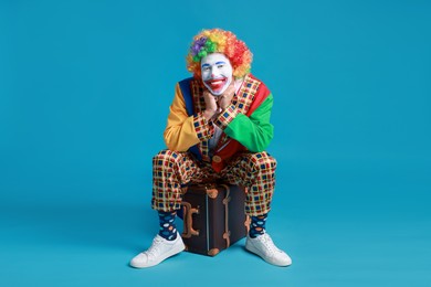 Happy clown sitting on suitcase against blue background