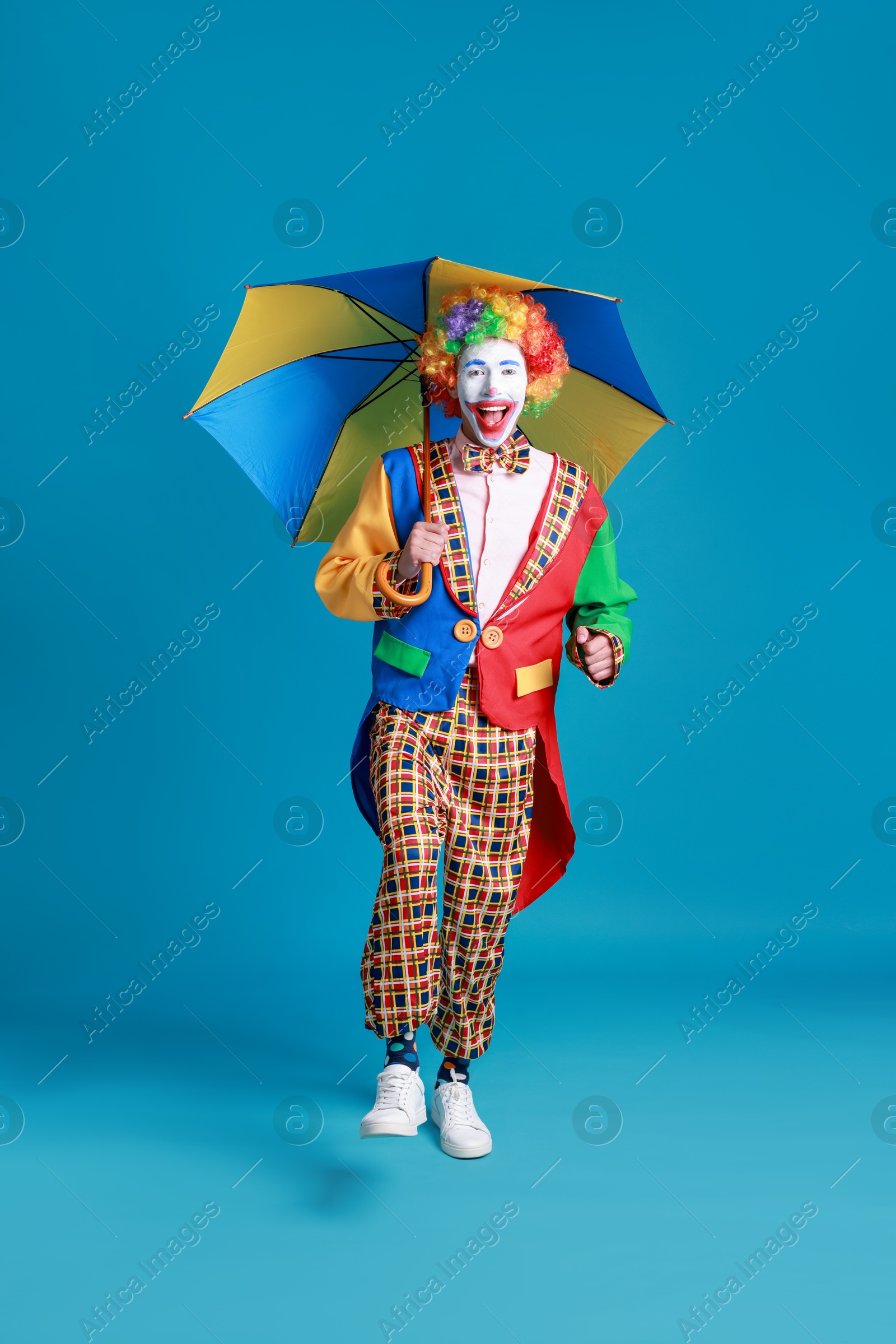 Photo of Clown with colorful umbrella on blue background