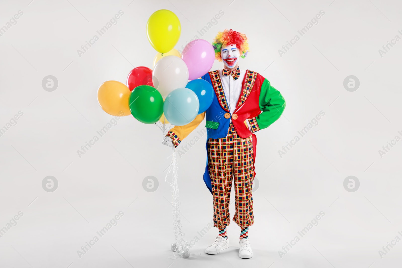 Photo of Happy clown with colorful balloons on light background