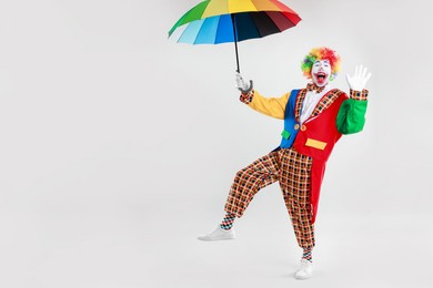 Photo of Happy clown with colorful umbrella on light background, space for text