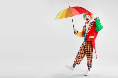 Happy clown with colorful umbrella on light background, space for text