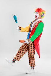 Photo of Funny clown juggling clubs on light background