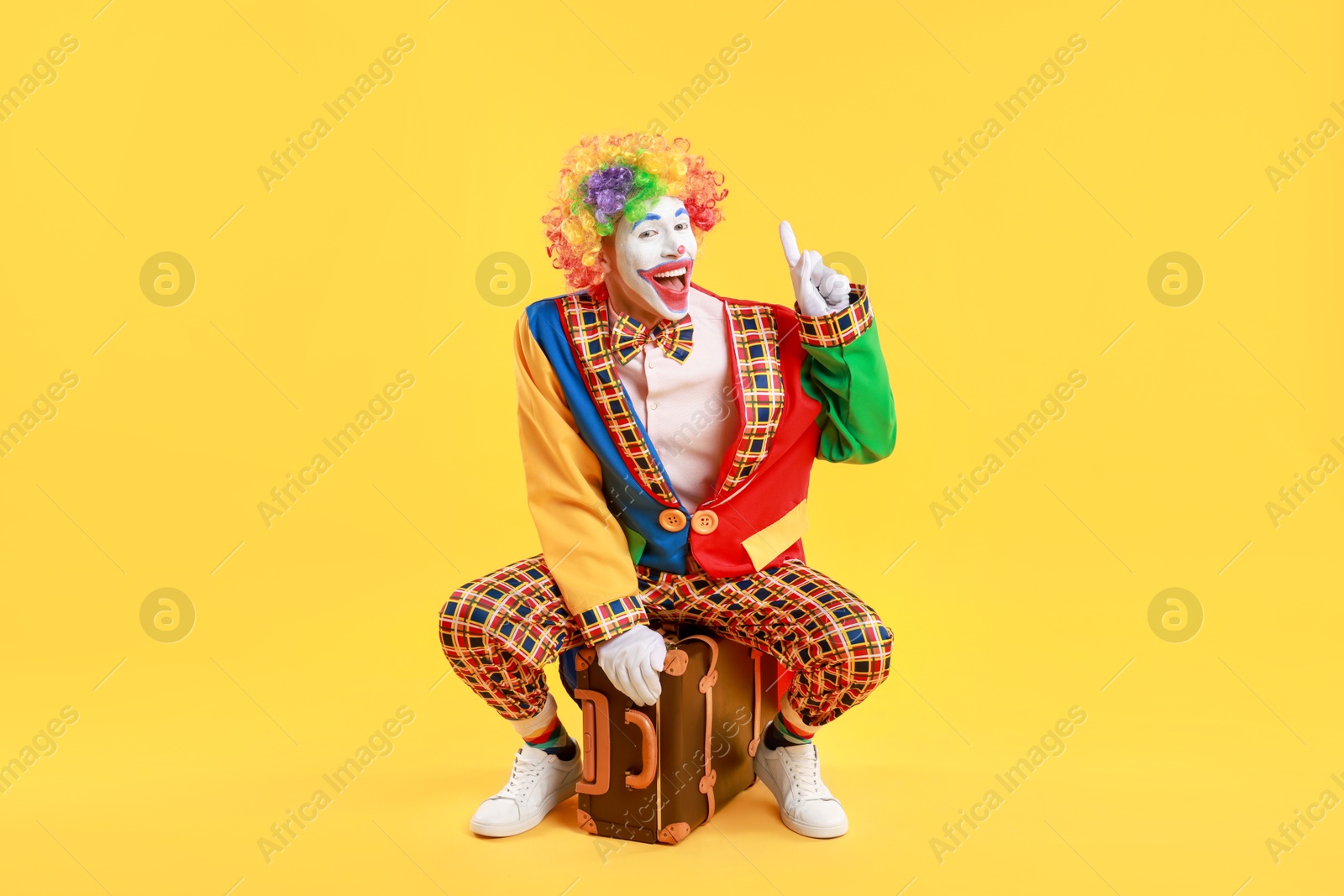 Photo of Happy clown with suitcase on yellow background