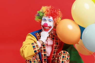 Happy clown with colorful balloons on red background