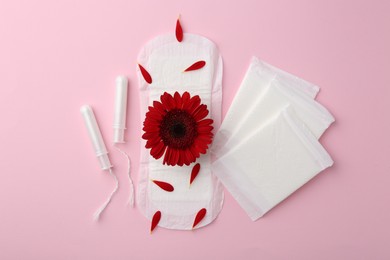 Photo of Menstrual pads, red flower and tampons on pink background, flat lay