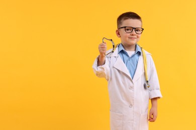 Photo of Little boy with stethoscope pretending to be doctor on yellow background, space for text. Dreaming of future profession