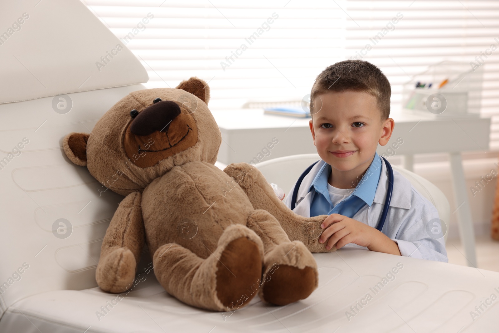 Photo of Little boy with stethoscope, syringe and toy pretending to be doctor indoors