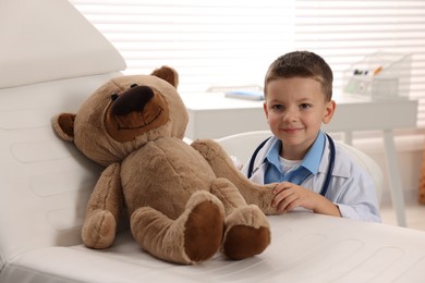 Photo of Little boy with stethoscope, syringe and toy pretending to be doctor indoors