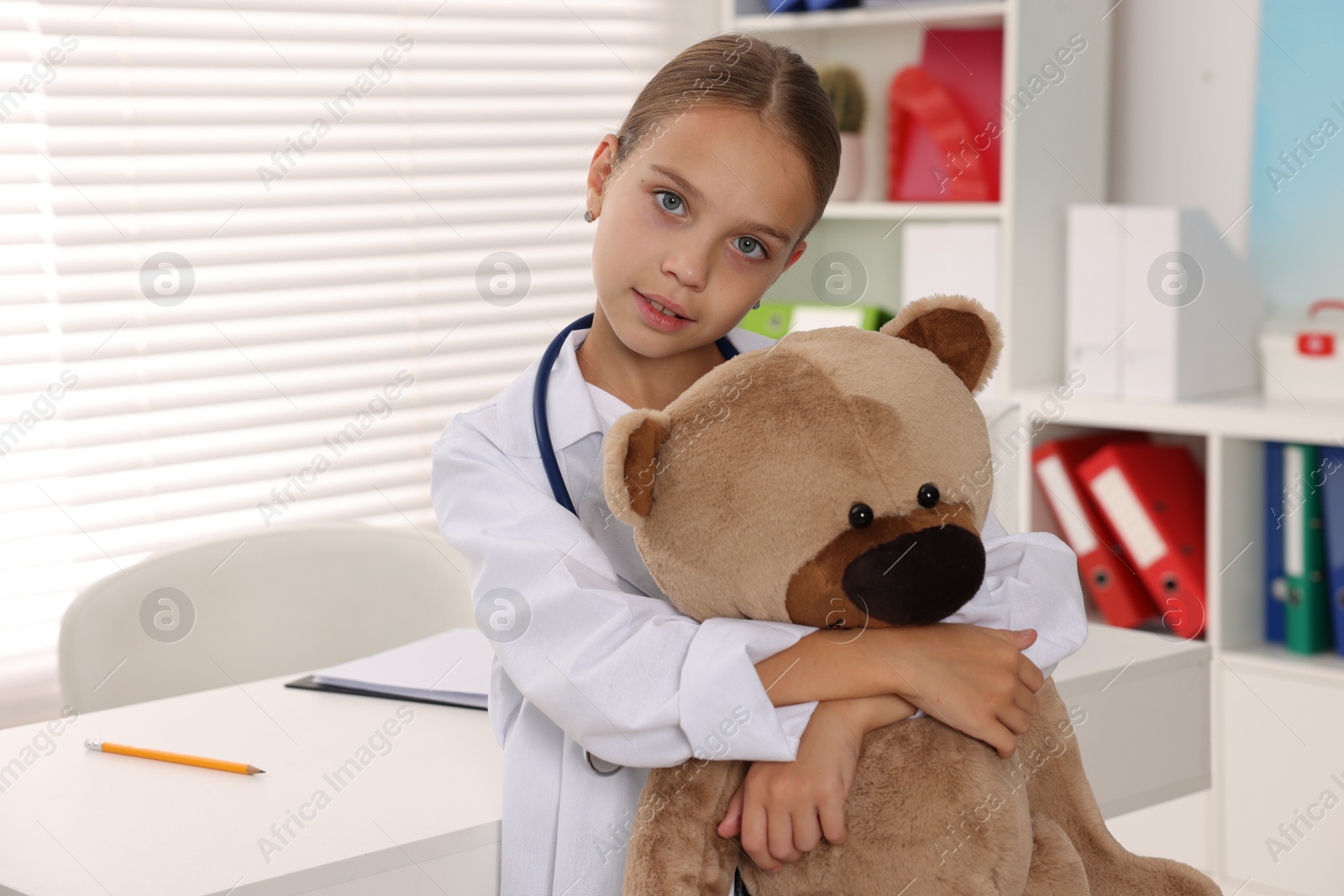 Photo of Girl with stethoscope and toy pretending to be doctor indoors