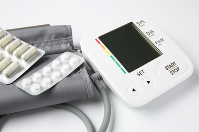 Photo of Blood pressure measuring device and pills on white background, closeup