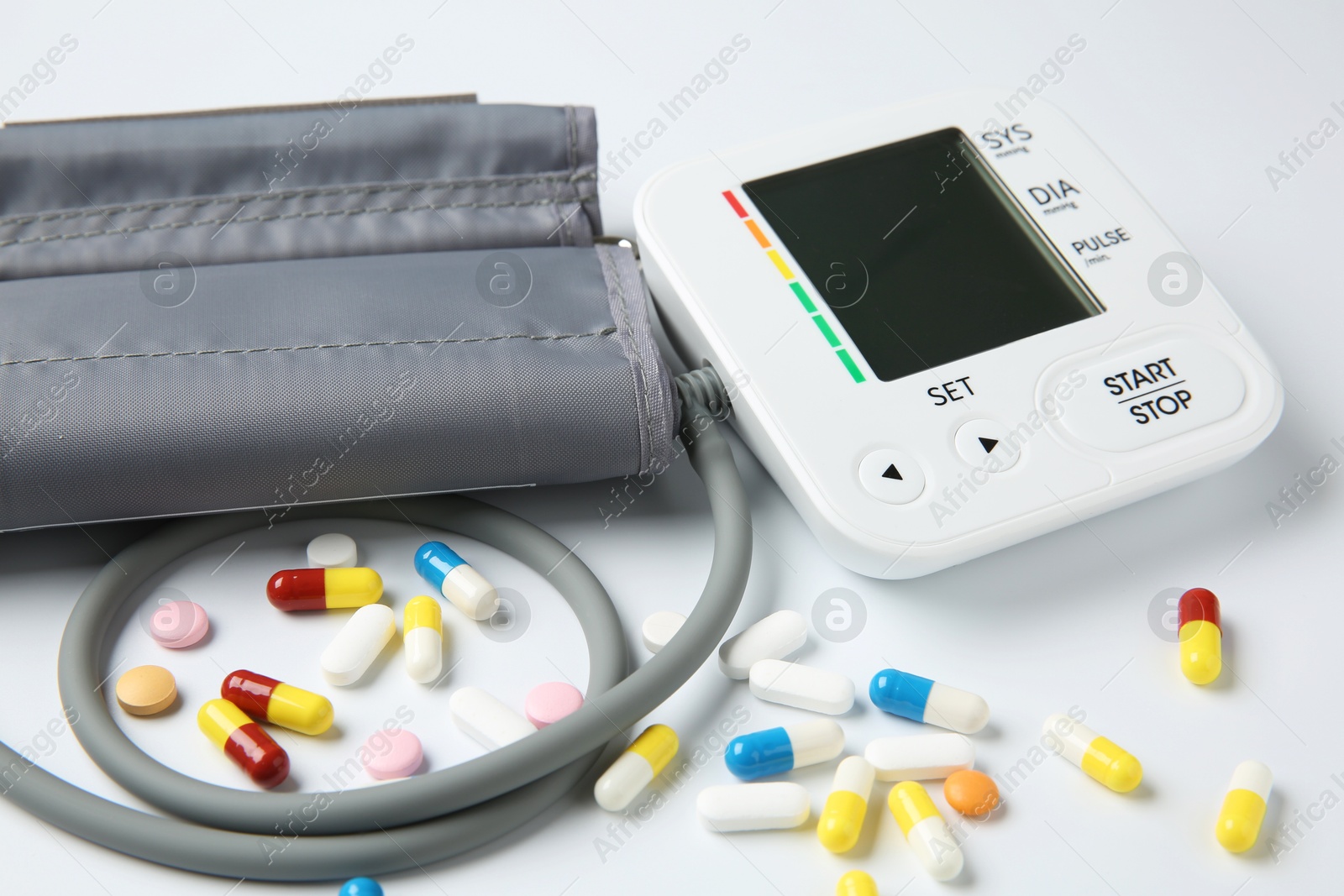 Photo of Blood pressure measuring device and pills on white background, closeup