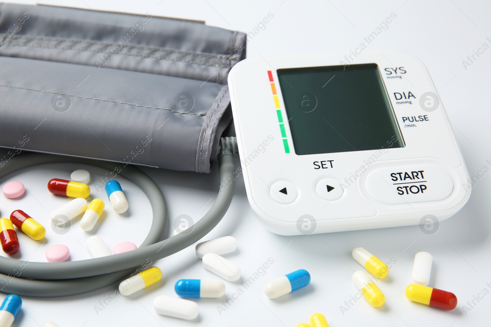 Photo of Blood pressure measuring device and pills on white background, closeup