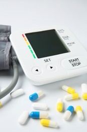 Photo of Blood pressure measuring device and pills on white background, closeup