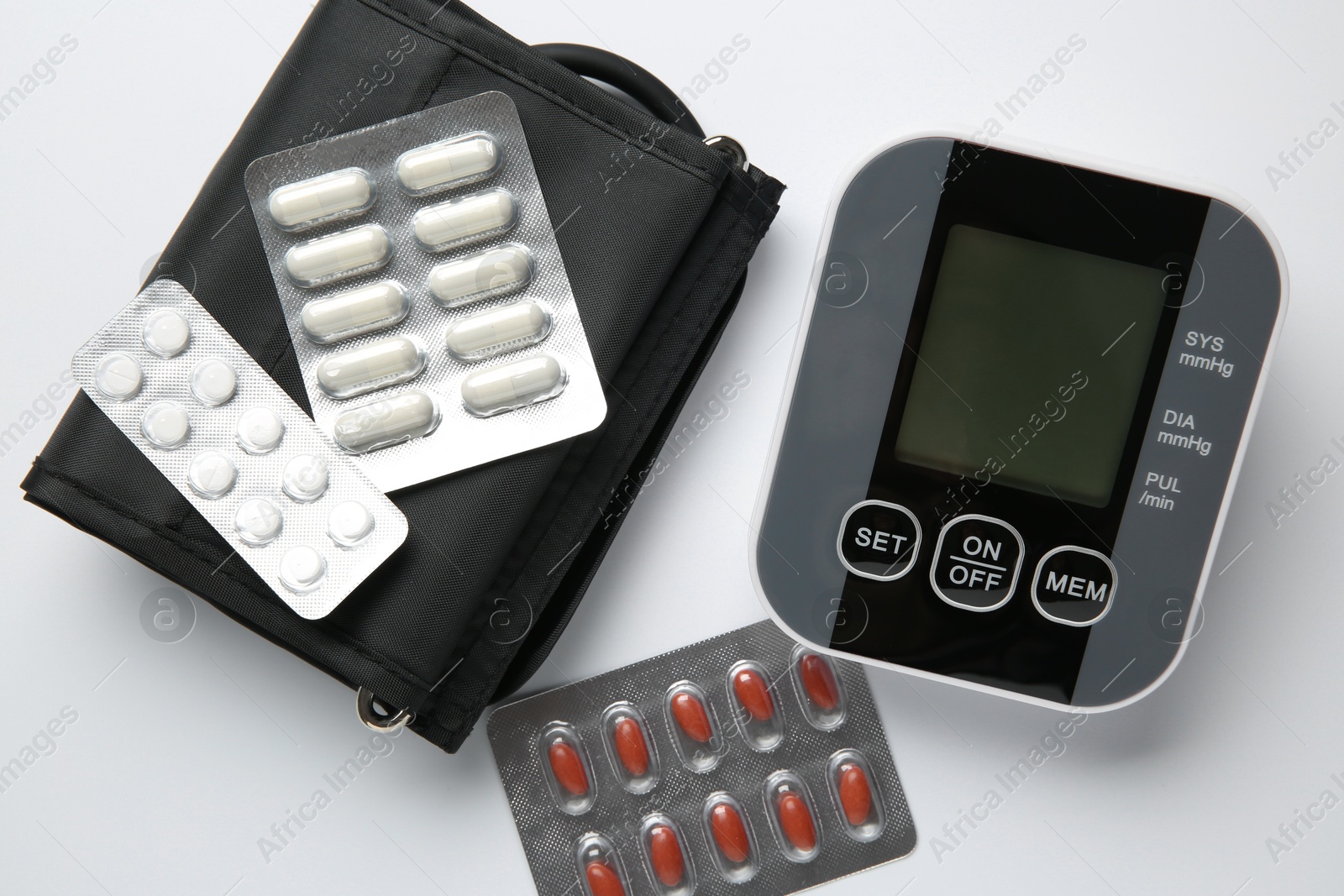 Photo of Blood pressure measuring device and pills on white background, top view