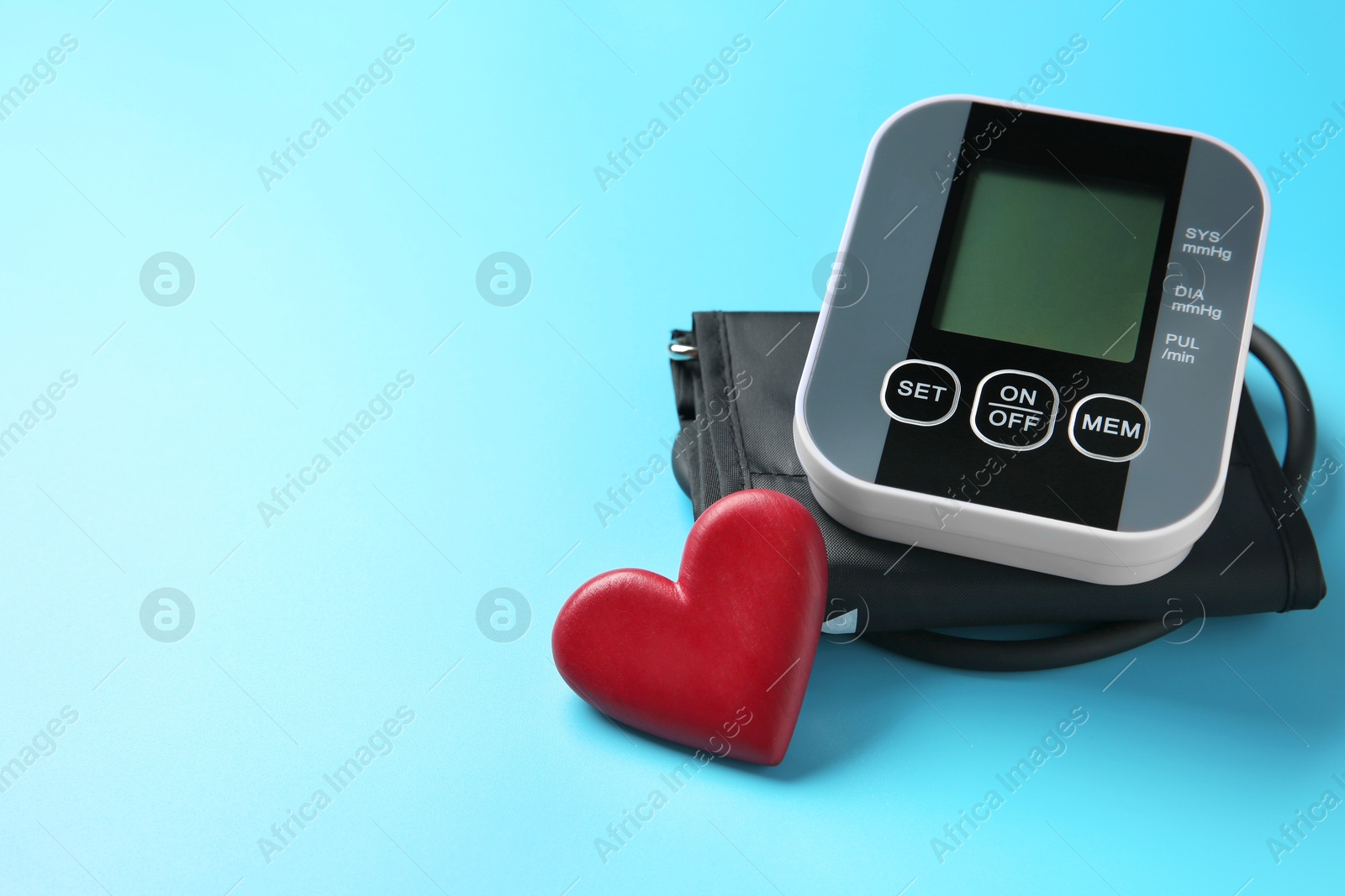 Photo of Blood pressure measuring device and heart figure on light blue background, space for text