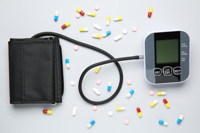 Photo of Blood pressure measuring device and pills on light grey background, top view