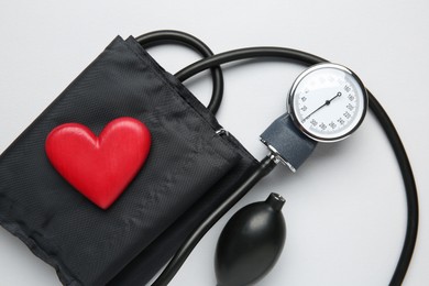 Photo of Blood pressure measuring device and heart figure on light grey background, top view