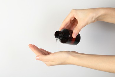 Woman pouring shampoo onto hand on grey background, closeup