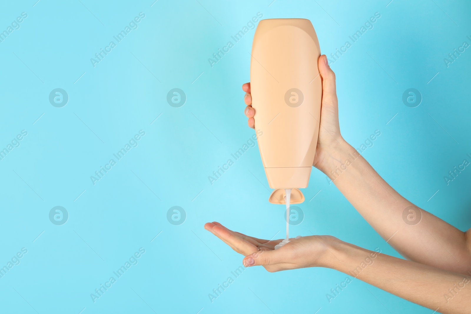 Photo of Woman pouring shampoo onto hand on light blue background, closeup. Space for text