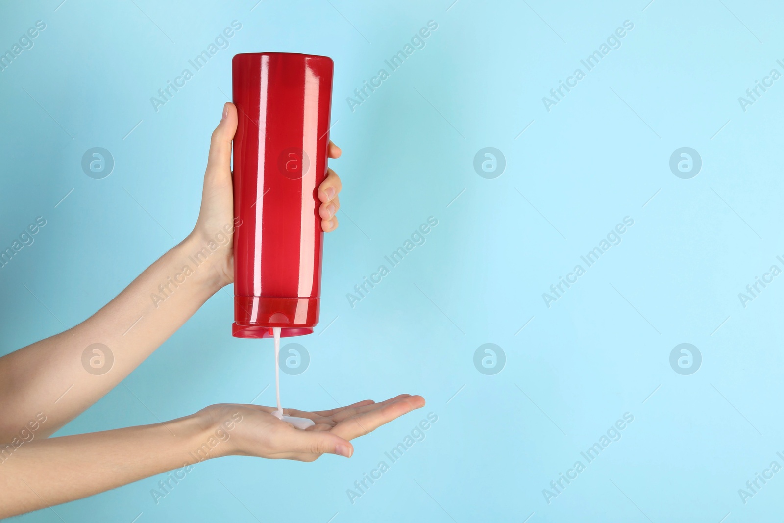 Photo of Woman pouring shampoo onto hand on light blue background, closeup. Space for text