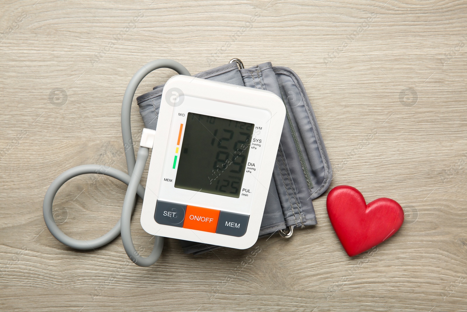 Photo of Blood pressure measuring device and heart figure on wooden table, top view