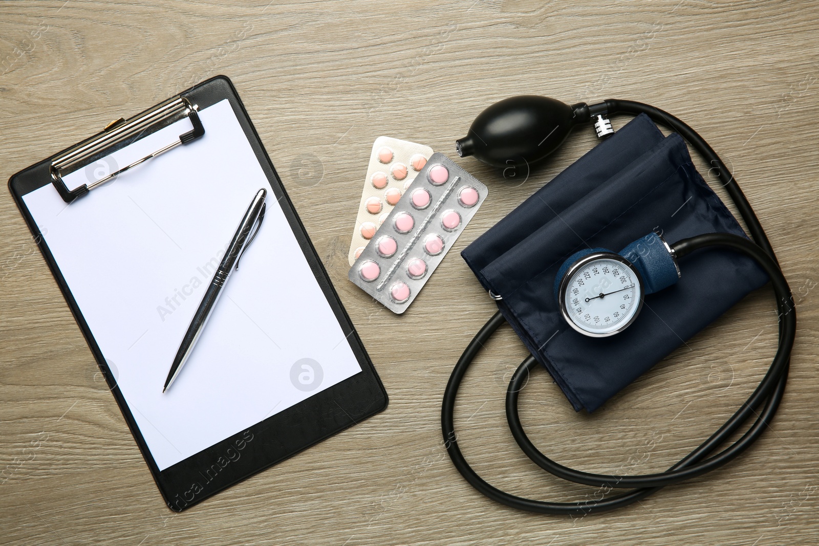 Photo of Blood pressure measuring device, pills and clipboard on wooden table, top view