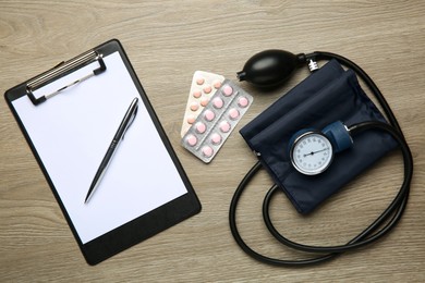 Blood pressure measuring device, pills and clipboard on wooden table, top view