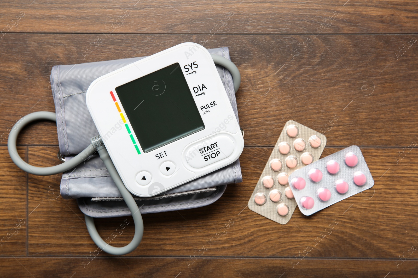 Photo of Blood pressure measuring device and pills on wooden table, top view