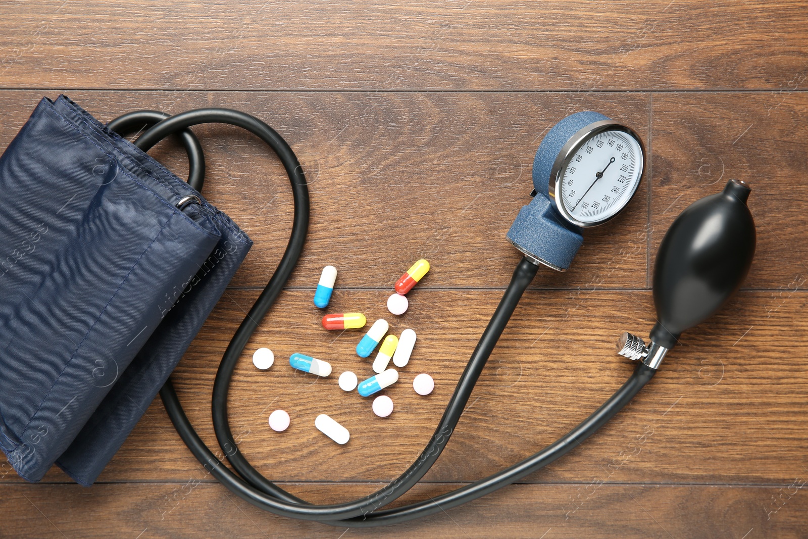 Photo of Blood pressure measuring device and pills on wooden table, top view