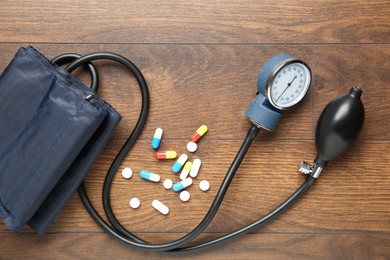 Photo of Blood pressure measuring device and pills on wooden table, top view