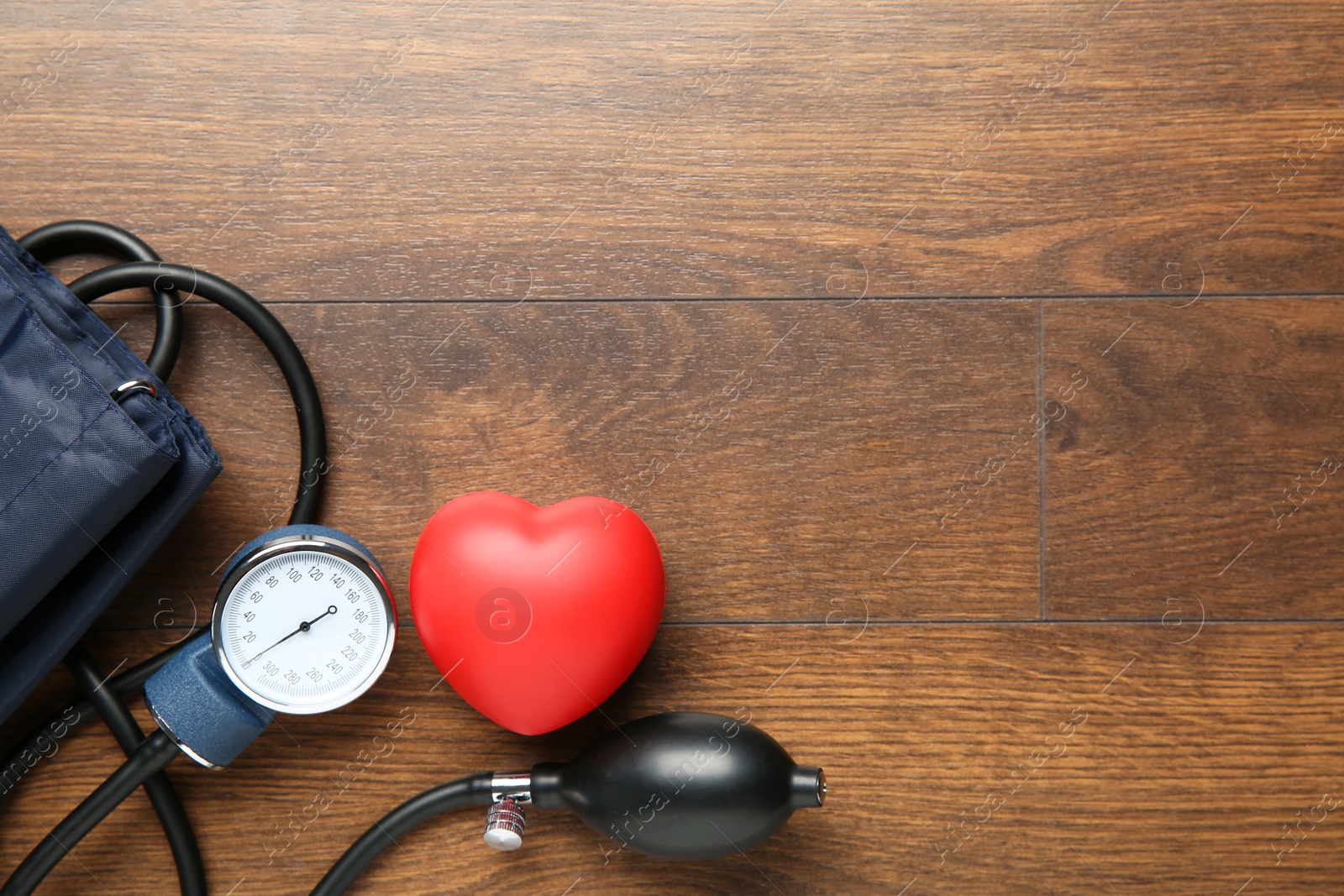 Photo of Blood pressure measuring device and squeeze heart on wooden table, top view. Space for text