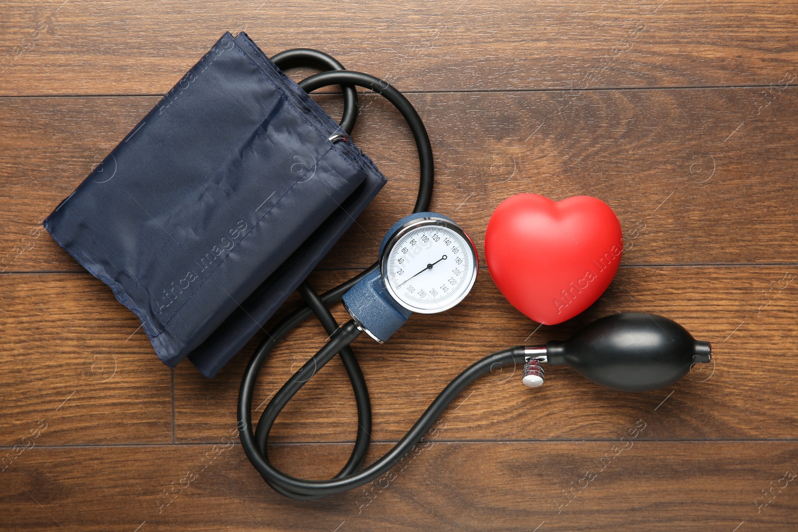 Photo of Blood pressure measuring device and squeeze heart on wooden table, top view