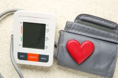 Photo of Blood pressure measuring device and heart figure on light textured background, closeup