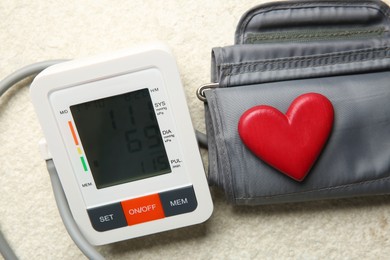 Photo of Blood pressure measuring device and heart figure on light textured background, closeup