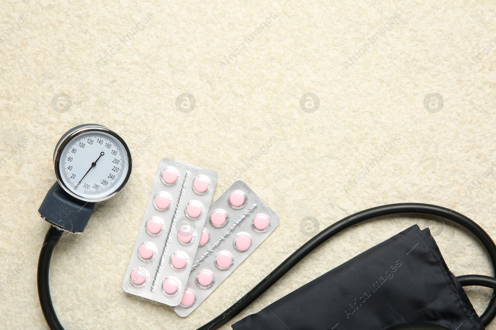 Photo of Blood pressure measuring device and pills on light textured background, top view. Space for text