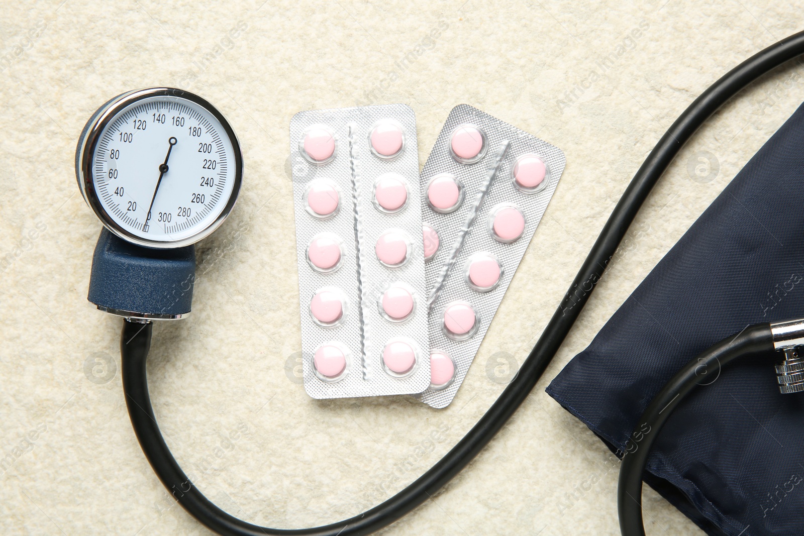 Photo of Blood pressure measuring device and pills on light textured background, top view