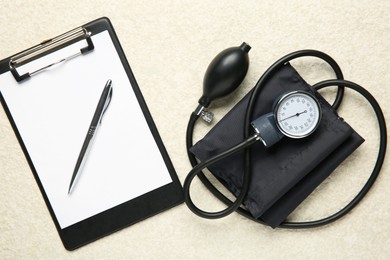 Blood pressure measuring device and clipboard on light textured background, top view