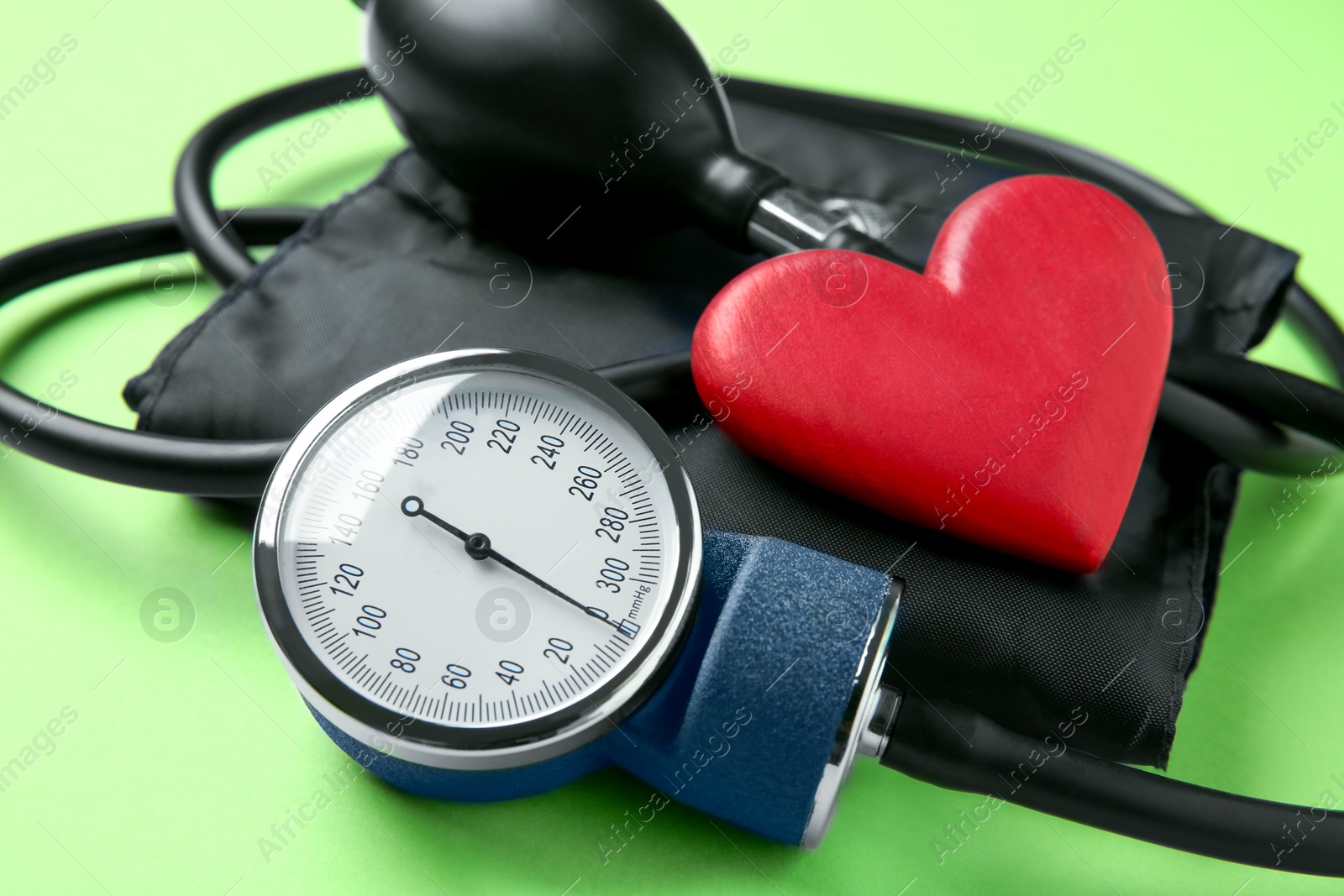 Photo of Blood pressure measuring device and heart figure on green background, closeup