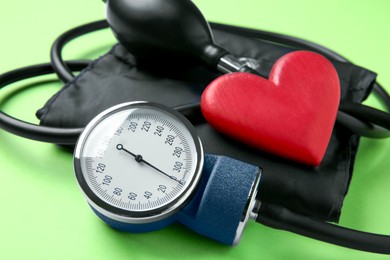 Photo of Blood pressure measuring device and heart figure on green background, closeup