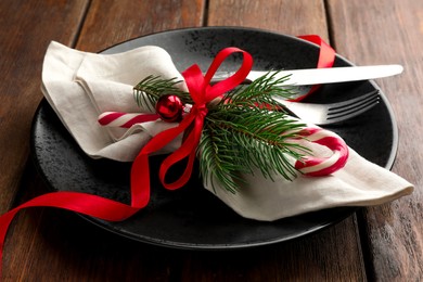 Photo of Christmas setting with plate, cutlery, fir branches and ribbon on wooden table, closeup