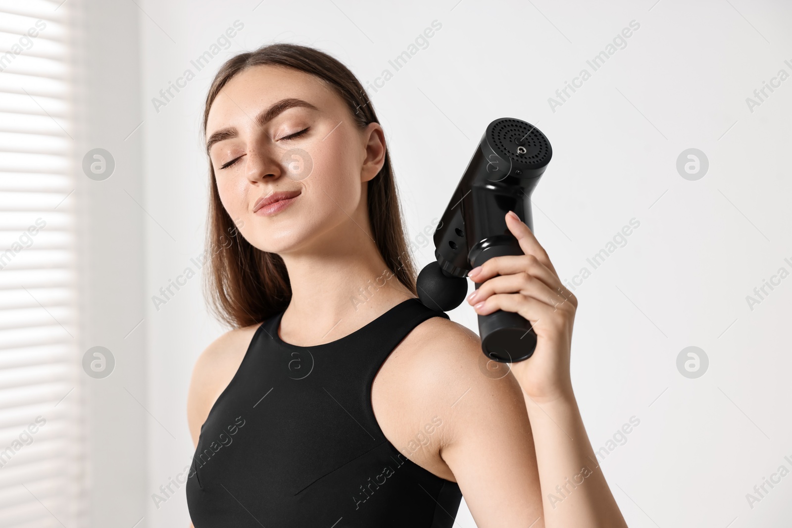 Photo of Woman using percussive massager to relieve trapezius muscle indoors