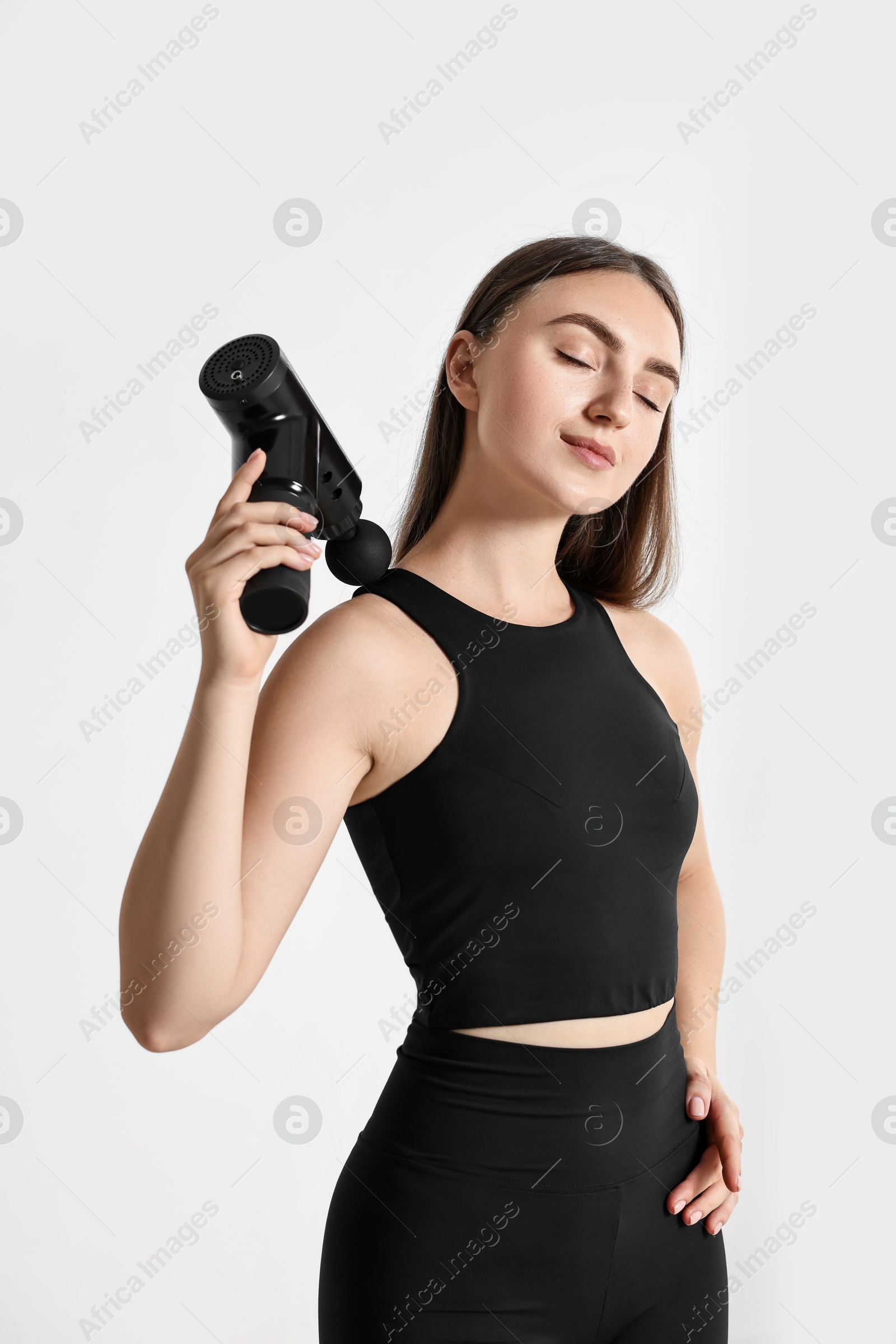 Photo of Woman using percussive massager to relieve trapezius muscle indoors