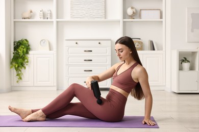 Woman using percussive massager to relieve hip muscles on mat at home