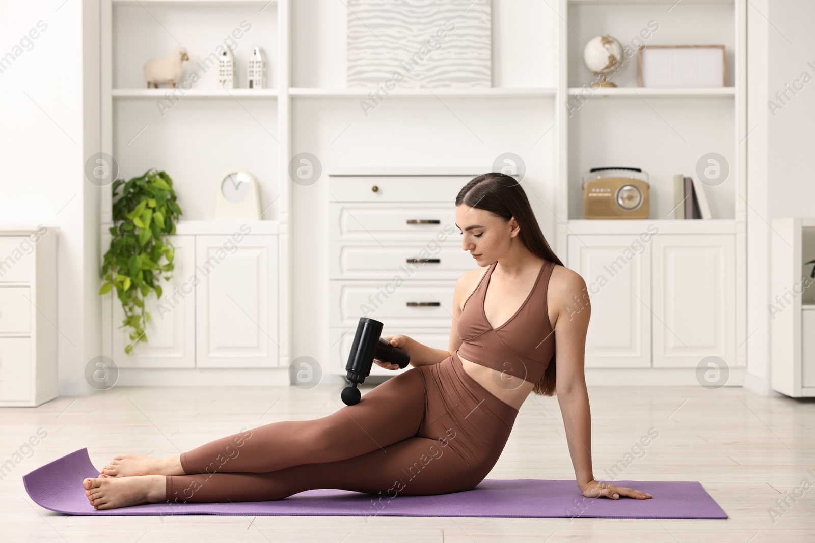 Photo of Woman using percussive massager to relieve hip muscles on mat at home