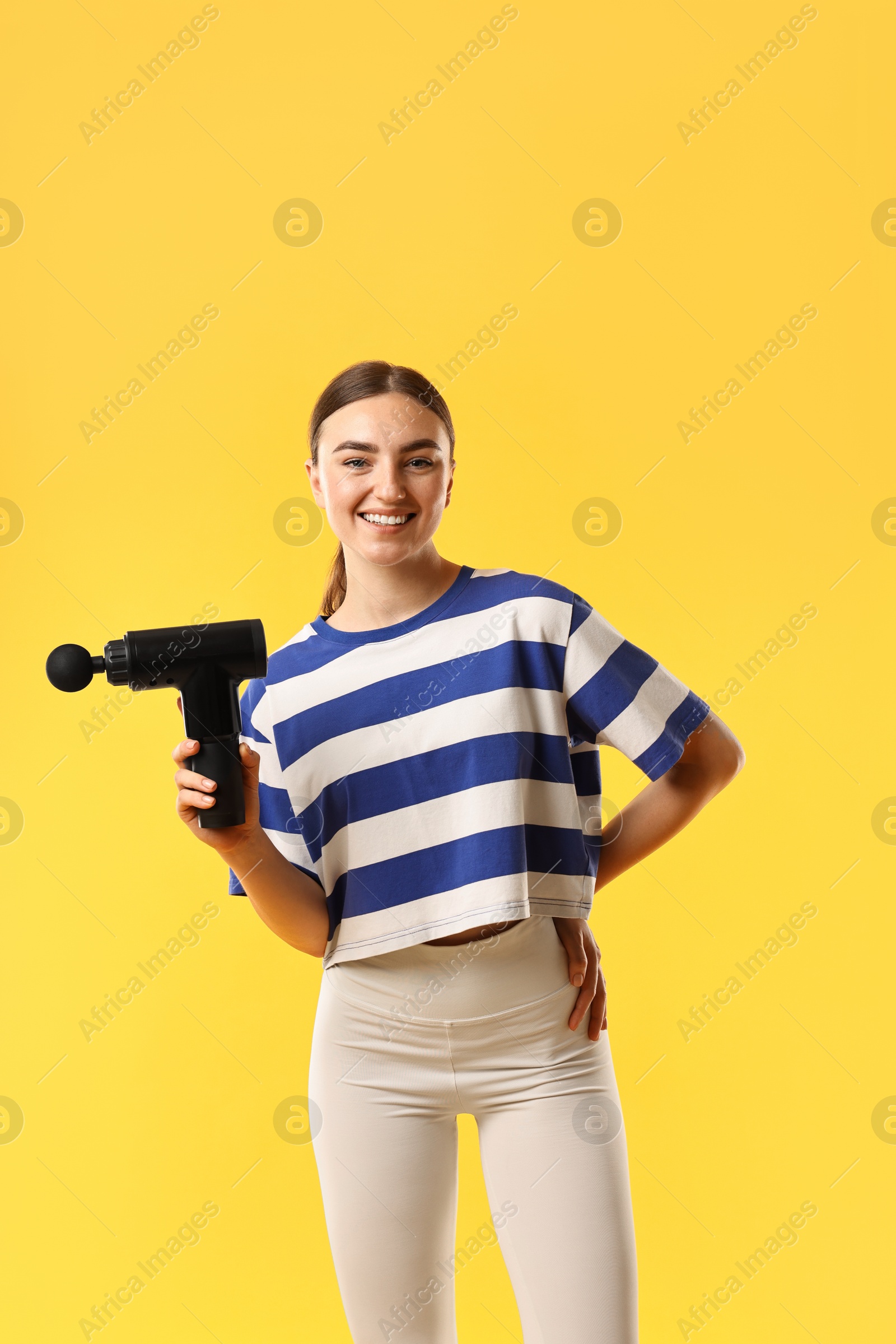 Photo of Young woman with percussive massager on yellow background