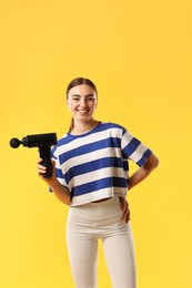 Young woman with percussive massager on yellow background